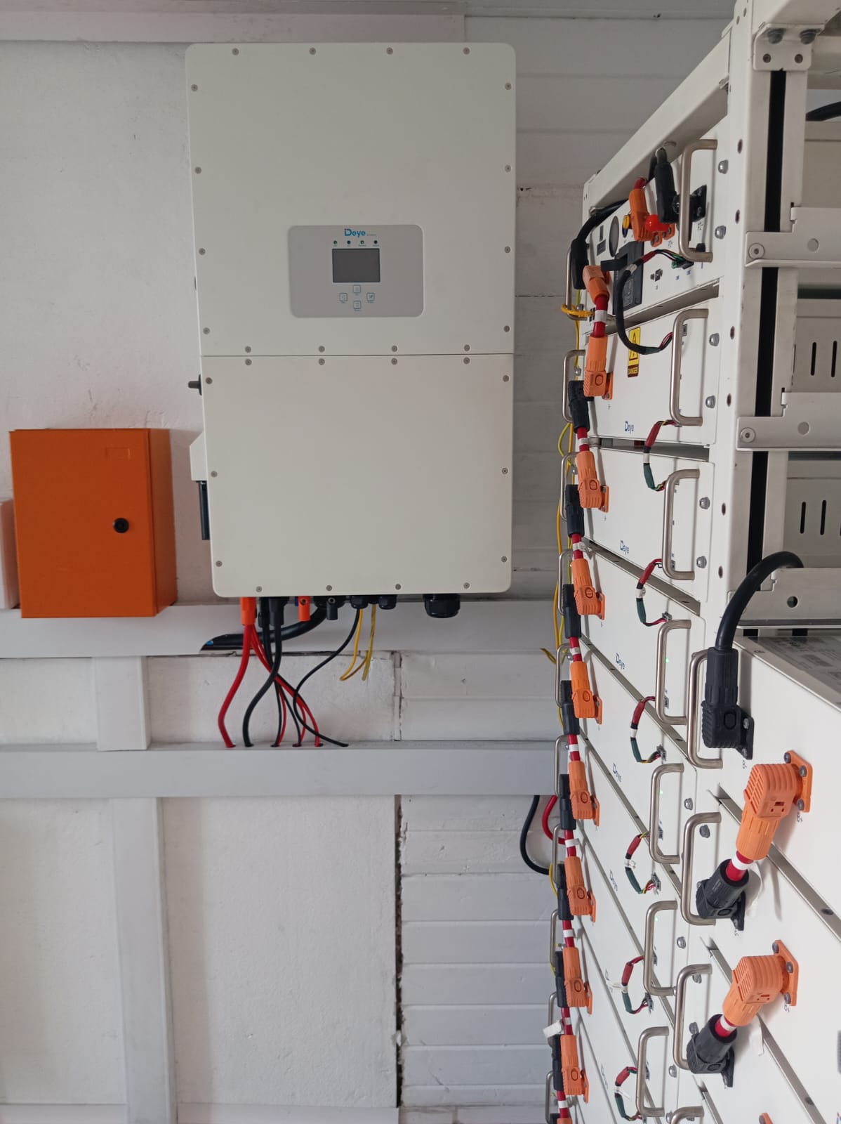 Deye commercial hybrid inverter above a multi-tier rack of Deye lithium-ion battery modules with orange high-voltage connectors